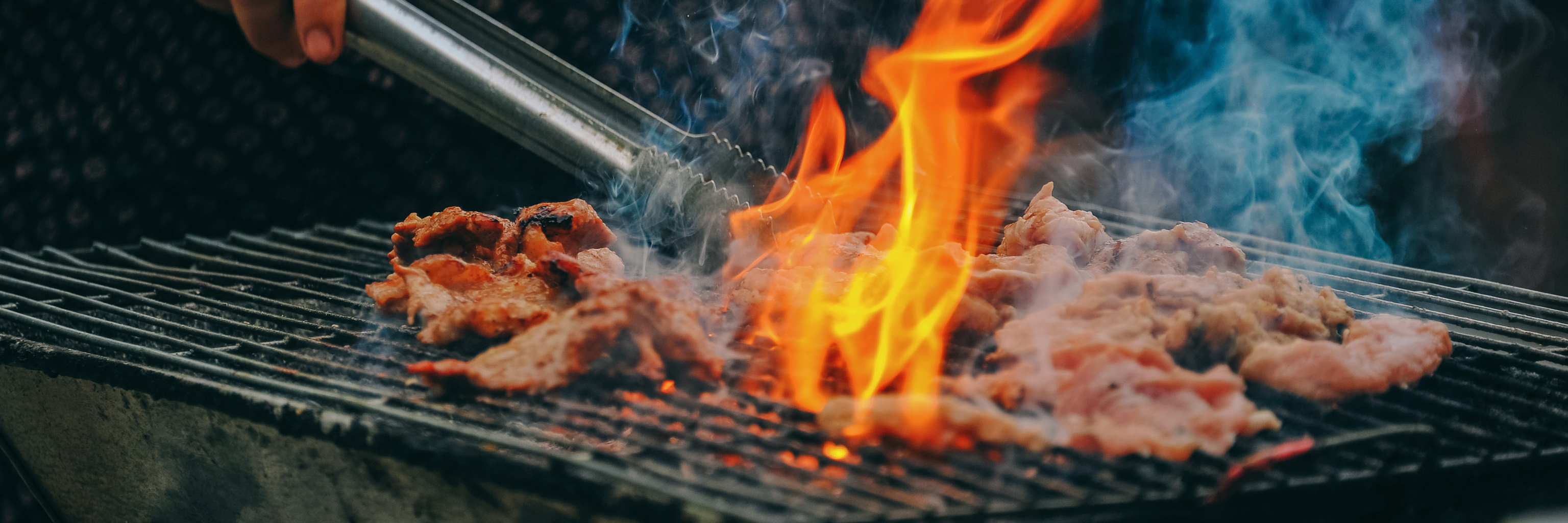 Meat being cooked on a fiery hot grill. 
