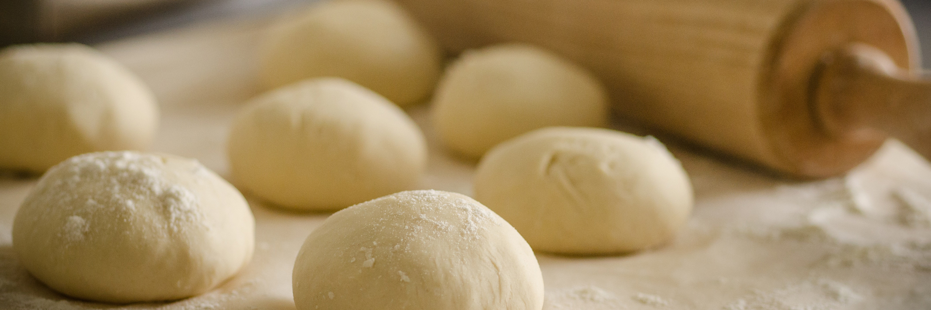 A rolling pin next to mounds of dough. 